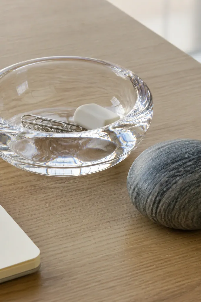 Clear glass catchall with a stone paperweight and a small tray on a light desk