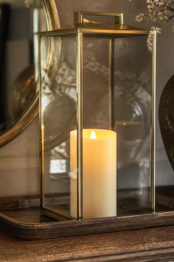 Glass lantern on a tray with a flameless candle and a small greenery sprig