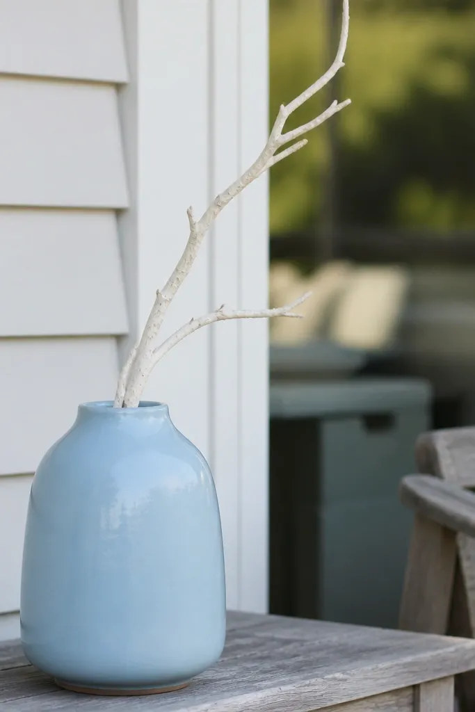 Pastel blue vase on a porch with one tall white stem arrangement